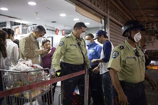 CORRECTS DAY - Police officers leave a supermarket after ordering it closed after finding costumers not wearing surgical masks to cover mouth and nose in Caracas, Venezuela, Sunday, March 15, 2020. Venezuelan President Nicol&aacute;s Maduro has ordered residents in the capital of Caracas and six states to stay home under a quarantine bid to control the spread of the coronavirus. (AP Photo/Ariana Cubillos)