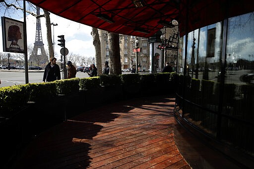 People look at an empty terrasse in Paris, Sunday, March 15, 2020. French Prime Minister Edouard Philippe announced that France is shutting down all restaurants, cafes, cinemas and non-essential retail shops, starting Sunday, to combat the accelerated spread of the virus in the country. For most people, the new coronavirus causes only mild or moderate symptoms. For some it can cause more severe illness. (AP Photo/Christophe Ena)