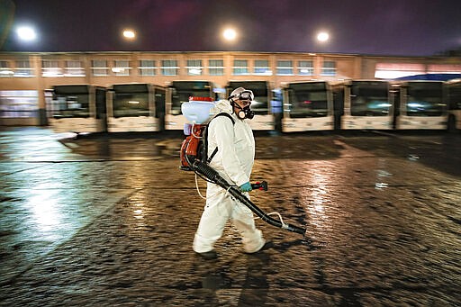 An employee of the pubic transport company wearing protective equipment walks during the daily disinfection of busses, part of the procedures to limit the spread of the coronavirus, in the early morning hours in Bucharest, Romania, Sunday, March 15, 2020. For most people, the new coronavirus causes only mild or moderate symptoms. For some it can cause more severe illness. (AP Photo/Vadim Ghirda)