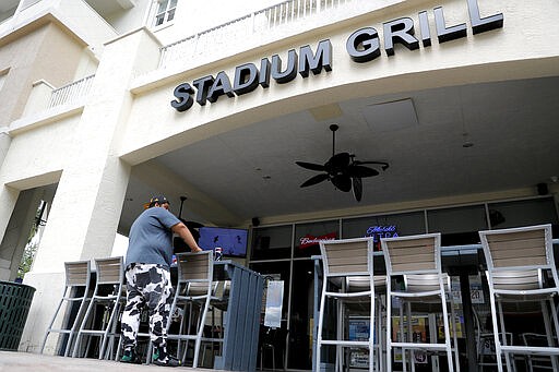 A person stands near empty seats at Stadium Grill, Monday, March 16, 2020, in Jupiter, Fla. The restaurant, which is across the street from Roger Dean Chevrolet Stadium, the spring training baseball home of the St. Louis Cardinals and the Miami Marlins, is normally full with customers on game day. On Sunday night, the Centers for Disease Control and Prevention recommended gatherings of 50 people or more be canceled or postponed across the country for the next eight weeks. Major League Baseball planned to update teams Monday on its health policy. (AP Photo/Julio Cortez)