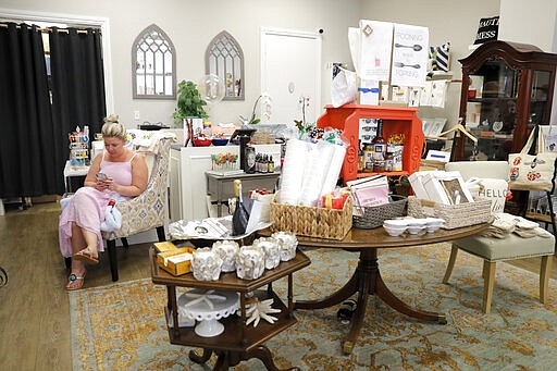 Taylor Alderton, owner of Palm Harbor Boutique, pecks on a cell phone while she sits in her deserted store, Monday, March 16, 2020, in Jupiter, Fla. The store, which is across the street from Roger Dean Chevrolet Stadium, the spring training baseball home of the St. Louis Cardinals and the Miami Marlins, is normally full with customers on game day. On Sunday night, the Centers for Disease Control and Prevention recommended gatherings of 50 people or more be canceled or postponed across the country for the next eight weeks. Major League Baseball planned to update teams Monday on its health policy. (AP Photo/Julio Cortez)