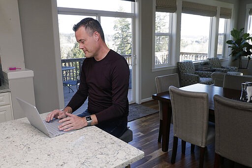 Neal Browning works on his laptop in the kitchen of his home, Monday, March 16, 2020, in Bothell, Wash., north of Seattle. Earlier in the day, Browning, who is a network engineer at Microsoft, was the second person to receive a shot of a potential vaccine for the COVID-19 coronavirus at the start of the first-stage safety study clinical trial of the vaccine at the Kaiser Permanente Washington Research Institute in Seattle. (AP Photo/Ted S. Warren)