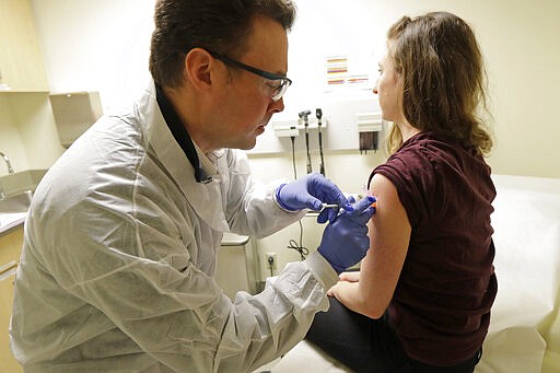 Pharmacist Michael Witte, left, gives Rebecca Sirull, right, a shot in the first-stage safety study clinical trial of a potential vaccine for COVID-19, the disease caused by the new coronavirus, Monday, March 16, 2020, at the Kaiser Permanente Washington Health Research Institute in Seattle. Sirull is the third patient to receive the shot in the study. (AP Photo/Ted S. Warren)