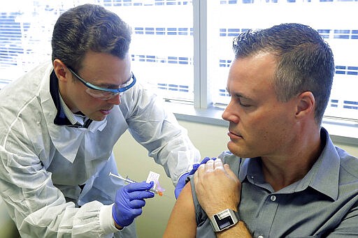 Pharmacist Michael Witte, left, gives Neal Browning a shot in the first-stage study of a potential coronavirus vaccine Monday, March 16, 2020, at the Kaiser Permanente Washington Health Research Institute in Seattle. Browning is the second patient to receive the shot in the study. (AP Photo/Ted S. Warren)