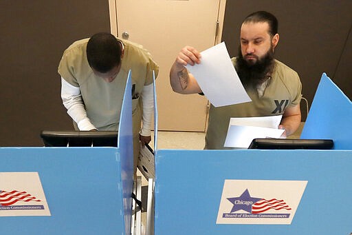 In this Saturday, March 14, 2020 photo, Cook County jail inmates Vincent Smith, left, and Ioan L'ela participate in early voting for the March 17, Illinois primary at the jail in Chicago. (AP Photo/Charles Rex Arbogast)