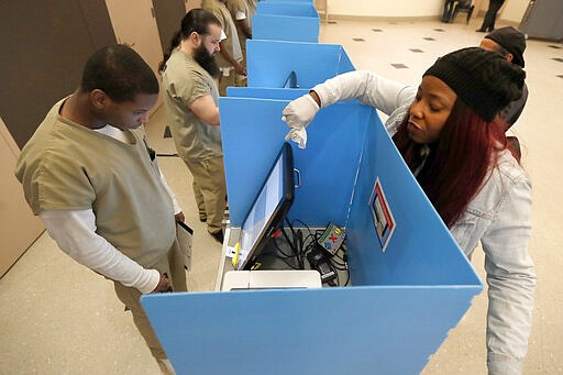 In this Saturday, March 14, 2020, photo, Denise Arnold, right, an early voting election official with the Chicago Board of Elections, helps Cook County jail inmate Vincent Smith as he participates in early voting for the March 17 Illinois primary in Chicago. (AP Photo/Charles Rex Arbogast)