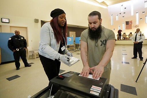 In this Saturday, March 14, 2020 photo, Denise Arnold, left, an early voting election official with the Chicago Board of Elections, helps Cook County jail inmate Ioan L'ela cast his ballot as he participates in early voting in the March 17, Illinois primary in Chicago. (AP Photo/Charles Rex Arbogast)