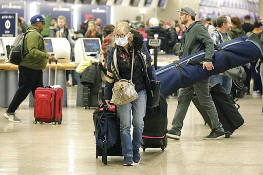 A masked traveler walks from the ticket counter at the Salt Lake City International Airport Sunday, March 15, 2020, in Salt Lake City. For most people, the new coronavirus causes only mild or moderate symptoms, such as fever and cough. For some, especially older adults and people with existing health problems, it can cause more severe illness, including pneumonia. (AP Photo/Rick Bowmer)