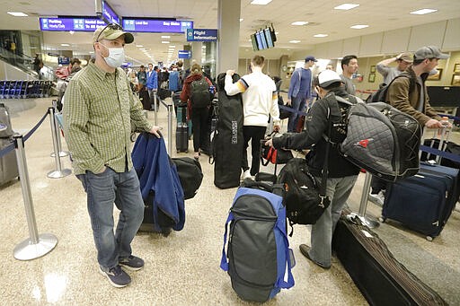 A masked traveler stands in line with his luggage before getting to the ticket counter at the Salt Lake City International Airport Sunday, March 15, 2020, in Salt Lake City. (AP Photo/Rick Bowmer)