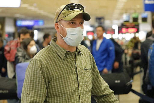 A masked traveler stands in line with his luggage before getting to the ticket counter at the Salt Lake City International Airport Sunday, March 15, 2020, in Salt Lake City. For most people, the new coronavirus causes only mild or moderate symptoms, such as fever and cough. For some, especially older adults and people with existing health problems, it can cause more severe illness, including pneumonia.(AP Photo/Rick Bowmer)