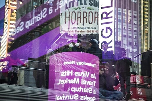 Tourists wear face masks as news about the coronavirus is seen in a reflection off a glass surface in New York's Times Square, March 15, 2020. (AP Photo/Wong Maye-E)