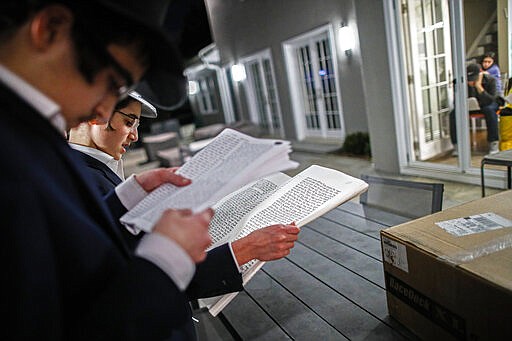 Yirmeyahu Gourarie performs a Purim reading from the Book of Esther for residents under self-quarantine due to potential exposure to the new coronavirus, March 9, 2020, in New Rochelle, N.Y. In Westchester County, student volunteers from a Jewish secondary school were fanning out in teams to read the megillah on Monday evening and during the day Tuesday outside the homes of about 120 families from the community who are quarantined. (AP Photo/John Minchillo)