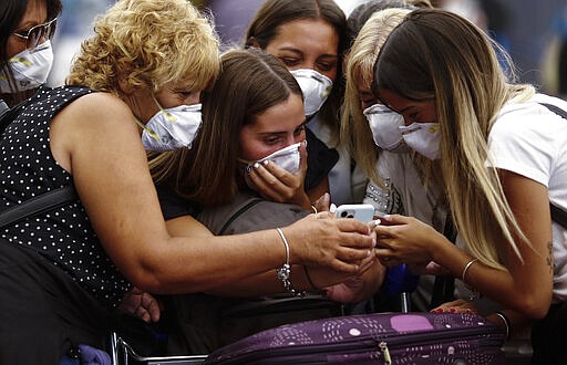 Travelers wearing protective masks look at a smart phone at the Ministro Pistarini International Airport, in Ezeiza on the outskirts of Buenos Aires, Argentina, Friday, March 13, 2020. Starting next Tuesday, Argentina is banning flights from the U.S., Europe and China, as a precaution against the spread of the new coronavirus. The vast majority of people recover from the new virus. (AP Photo/Marcos Brindicci)