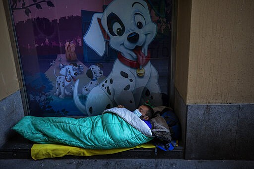 A homeless man wearing a mask sleeps in the doorway of a building, in Barcelona, Spain, March 15, 2020. (AP Photo/Emilio Morenatti)