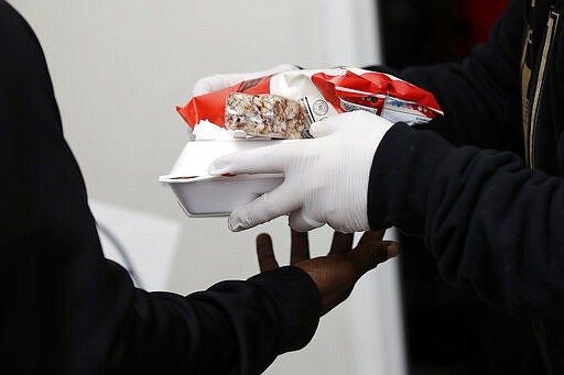 A volunteer uses rubber gloves while handing out lunches at a food distribution center set up by the Dream Center for those in need due to the coronavirus outbreak, Monday, March 16, 2020, in Los Angeles. (AP Photo/Marcio Jose Sanchez)