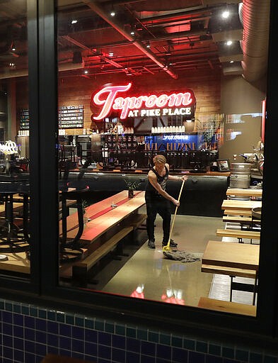 Tyler Baldwin mops the floor after closing for the night at the Taproom at Pike Place, Sunday, March 15, 2020 where he works as a bartender in Seattle. Washington Gov. Jay Inslee said Sunday night that he would order all bars, restaurants, entertainment and recreation facilities in the state to temporarily close to fight the spread of the COVID-19 coronavirus, as Washington state has by far the most deaths in the U.S. from the disease. Baldwin said he closed more than an hour early Sunday after he heard the announcement. (AP Photo/Ted S. Warren)