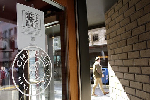 A sign indicating that only carry-out or delivery options are available hangs in the window of a closed Chipotle restaurant in Portland, Ore., Monday, March 16, 2020. Gov. Kate Brown announced a four-week ban on eat-in dining at bars and restaurants throughout the state on Monday to slow the spread of the new coronavirus in Oregon. Restaurants can still offer take-out and delivery. (AP Photo/Gillian Flaccus)