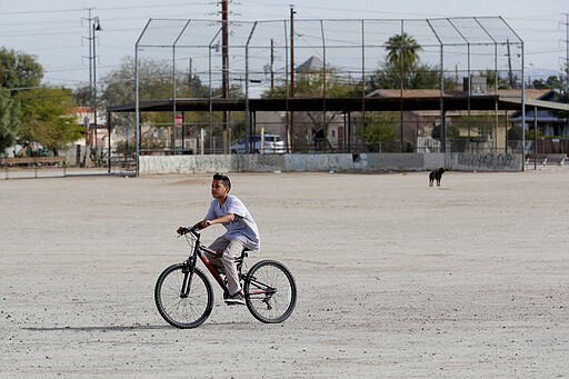 A boy rides his bike Friday, Jan. 24, 2020 in Guadalupe, Ariz. Founded by Yaqui Indian refugees from Mexico more than a century ago, Guadalupe is named for Mexico's patron saint, Our Lady of Guadalupe, and is fiercely proud of its history. The town known for sacred Easter rituals featuring deer-antlered dancers also is wary of outsiders as it prepares for the 2020 census. (AP Photo/Matt York)