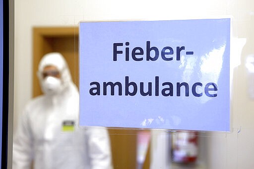 A person in protective gear stands behind a sign reading 'Feaver Ambulance' in the reception area of the fever outpatient clinic in Wernigerode, Germany, Monday, March 16, 2020. For most people, the new coronavirus causes only mild or moderate symptoms, such as fever and cough. For some, especially older adults and people with existing health problems, it can cause more severe illness, including pneumonia. (Matthias Bein/dpa via AP)