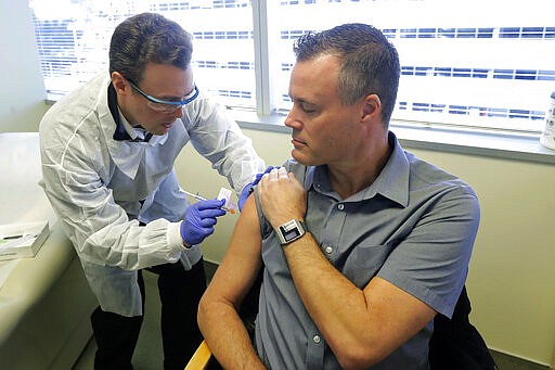 Pharmacist Michael Witte, left, gives Neal Browning, right, a shot in the first-stage safety study clinical trial of a potential vaccine for COVID-19, the disease caused by the new coronavirus Monday, March 16, 2020, at the Kaiser Permanente Washington Health Research Institute in Seattle. Browning is the second patient to receive the shot in the study. (AP Photo/Ted S. Warren)