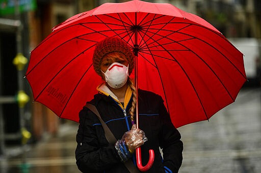 A woman wearing a mask protects herself from the rain with an umbrella, in Pamplona, northern Spain, Monday, March 16, 2020. After deploying the army to the streets and to clean train stations, ordering 46 million to stay at home and taking over control of private hospitals, the Spanish government is considering now closing the country's borders to halt the spread of the coronavirus. For most people, the new coronavirus causes only mild or moderate symptoms. For some, it can cause more severe illness, especially in older adults and people with existing health problems. (AP Photo/Alvaro Barrientos)