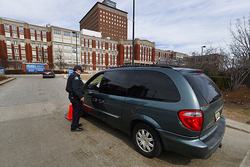 A security guard screens visitors before entering Henry Ford Hospital in Detroit, Monday, March 16, 2020. U.S. hospitals are setting up triage tents, calling doctors out of retirement, guarding their supplies of face masks and making plans to cancel elective surgery as they brace for an expected onslaught of coronavirus patients. (AP Photo/Paul Sancya)