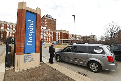 A security guard screens visitors before entering Henry Ford Hospital in Detroit, Monday, March 16, 2020. U.S. hospitals are setting up triage tents, calling doctors out of retirement, guarding their supplies of face masks and making plans to cancel elective surgery as they brace for an expected onslaught of coronavirus patients. (AP Photo/Paul Sancya)