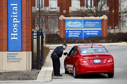 A security guard screens visitors before entering Henry Ford Hospital in Detroit, Monday, March 16, 2020. U.S. hospitals are setting up triage tents, calling doctors out of retirement, guarding their supplies of face masks and making plans to cancel elective surgery as they brace for an expected onslaught of COVID-19 and coronavirus patients. (AP Photo/Paul Sancya)