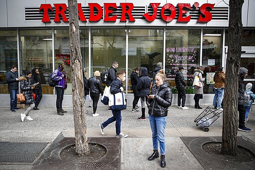 A pedestrian wearing a protective mask passes a line of customers outside a supermarket, Monday, March 16, 2020, in New York. New York leaders took a series of unprecedented steps Sunday to slow the spread of the coronavirus, including canceling schools and extinguishing most nightlife in New York City. (AP Photo/John Minchillo)