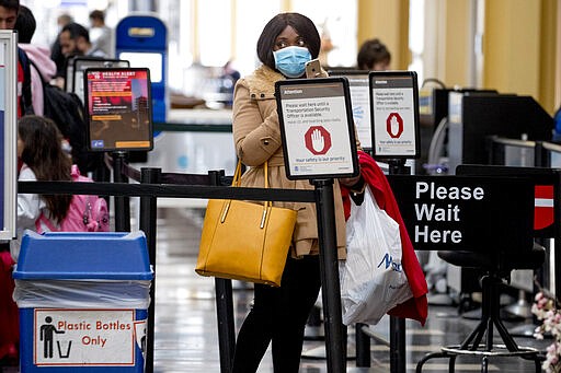 A woman wearing a mask walks goes through security at Ronald Reagan Washington National Airport, Monday, March 16, 2020, in Arlington, Va. (AP Photo/Andrew Harnik)