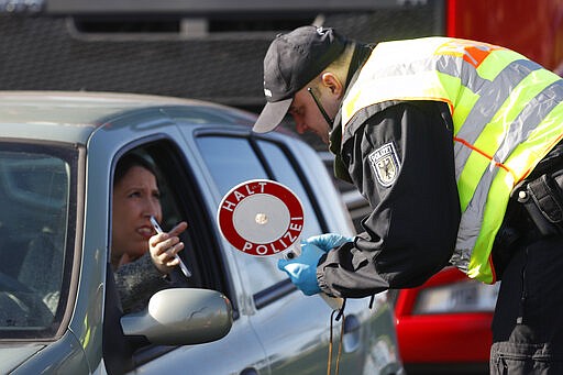 A German police officer checks authorization for a woman to enter Germany at the German-France border in Kehl, Monday March 16, 2020. Germany partially closes its borders with France, Switzerland, Austria, Luxembourg and Denmark as it steps up efforts to stem the spread of the new coronavirus. For most people, the new coronavirus causes only mild or moderate symptoms. For some it can cause more severe illness. (AP Photo/Jean-Francois Badias)