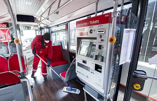 An employee of the Stadtwerke Gruppe Halle/Saale cleans and disinfects a bus of the Hallesche Verkehrs AG, the local public transport Halle/Saale, Germany, Monday, March 16, 2020. All of the local transport company's scheduled vehicles are thoroughly cleaned and disinfected every day. This applies in particular to contact surfaces such as handrails, handles, steering wheels and ticket machines. For most people, the new coronavirus causes only mild or moderate symptoms, such as fever and cough. For some, especially older adults and people with existing health problems, it can cause more severe illness, including pneumonia.. (Hendrik Schmidt/dpa via AP)