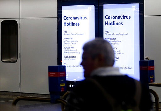 a person pass a display with &quot;Coronavirus Hotlines&quot; at the metro station in Vienna, Austria, Monday, March 16, 2020. The austrian government restricts freedom of movement. Only for most people, the new coronavirus causes only mild or moderate symptoms, such as fever and cough. For some, especially older adults and people with existing health problems, it can cause more severe illness, including pneumonia. (AP Photo/Ronald Zak)