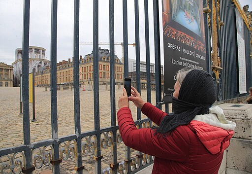 Eve an Australian tourist, who cover her face with a scarf and refused to be named with her family name, takes a cell phone photo of the closed Chateau de Versaille, west of Paris, Monday, March 16, 2020. France's government announced Saturday closing restaurants, bars and other establishments to limit the spread of the new coronavirus. For most people, the new coronavirus causes only mild or moderate symptoms, such as fever and cough. For some, especially older adults and people with existing health problems, it can cause more severe illness, including pneumonia. (AP Photo/Michel Euler)