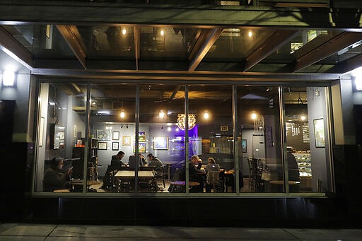 Customers sit in a dining area of Cafe Cosmos in downtown Seattle, Sunday, March 15, 2020. Washington Gov. Jay Inslee said Sunday night that he would order all bars, restaurants, entertainment and recreation facilities in the state to temporarily close to fight the spread of the COVID-19 coronavirus. Inslee said that restaurants could continue take-out and delivery services, the owner of the cafe said he would continue to offer take-out coffee and other food. (AP Photo/Ted S. Warren)