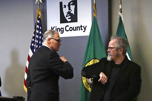 Washington Gov. Jay Inslee, left, gives an elbow touch to American Sign Language interpreter Terry Dockter after a news conference about the coronavirus outbreak Monday, March 16, 2020, in Seattle. Inslee ordered all bars, restaurants, entertainment and recreation facilities to temporarily close to fight the spread of COVID-19. (AP Photo/Elaine Thompson, Pool)