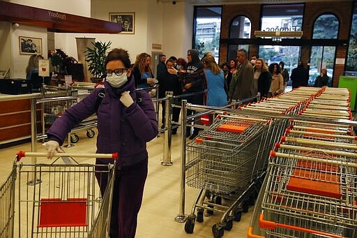 A woman wearing a face mask pushes a trolley as other customers wait in a queue to receive a card to allow them to shop at the supermarket in Athens, Monday, March 16, 2020. Greek supermarkets are restricting the flow of customers entering the premises in another attempt to prevent the spread of coronavirus. The vast majority of people recover from the new coronavirus. According to the World Health Organization, most people recover in about two to six weeks, depending on the severity of the illness. (AP Photo/Thanassis Stavrakis)