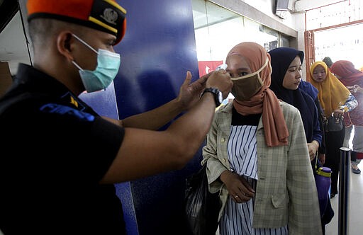 A security officer measures body temperatures of passengers before entering a train station during the coronavirus outbreak, in Medan, North Sumatra, Indonesia, Monday, March 16, 2020. For most people, the new coronavirus causes only mild or moderate symptoms. For some, it can cause more severe illness, especially in older adults and people with existing health problems. (AP Photo/Binsar Bakkara)