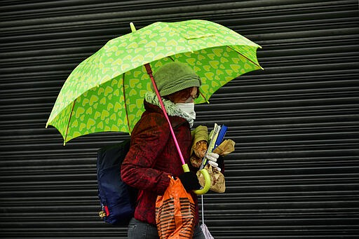 A woman wearing a mask carries bread as the rain falls in Pamplona, northern Spain, Monday, March 16, 2020. After deploying the army to the streets and to clean train stations, ordering 46 million to stay at home and taking over control of private hospitals, the Spanish government is considering now closing the country's borders to halt the spread of the coronavirus. For most people, the new coronavirus causes only mild or moderate symptoms. For some, it can cause more severe illness, especially in older adults and people with existing health problems. (AP Photo/Alvaro Barrientos)