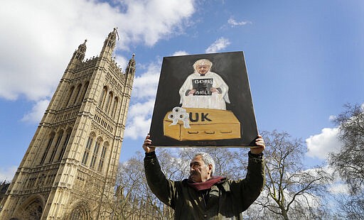 Artist Kaya Mar holds up a coronavirus themed painting with Prime Minister Boris Johnson in Westminster in London, Monday, March 16, 2020. For most people, the new coronavirus causes only mild or moderate symptoms, such as fever and cough. For some, especially older adults and people with existing health problems, it can cause more severe illness, including pneumonia.(AP Photo/Kirsty Wigglesworth)