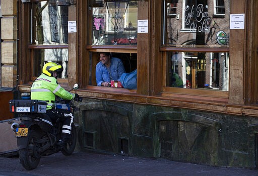 A police officer talks to a man in the closed Caf&eacute; Bar Old Sailor in the Red Light District of Amsterdam, Netherlands, Monday, March 16, 2020. Health minister Bruno Bruins ordered all Dutch schools, cafes, restaurants coffeeshops, saunas, sex clubs and sport and fitness clubs to be closed from Sunday March 15th onwards as the government sought to prevent the further spread of coronavirus in the Netherlands. For most people, the new coronavirus causes only mild or moderate symptoms, such as fever and cough. For some, especially older adults and people with existing health problems, it can cause more severe illness, including pneumonia. (AP Photo/Peter Dejong)