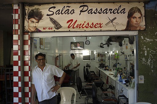 A hairdresser waits for customers at his shop in the the Rocinha slum of Rio de Janeiro, Brazil, Monday, March 16, 2020. Since the outbreak of the new coronavirus, nations have begun imposing travel restrictions and closing their borders to contain the pandemic's spread. The latest attempt to impose controls is a smaller territory: the hillside slum of Rocinha in Rio de Janeiro. (AP Photo/Silvia Izquierdo)