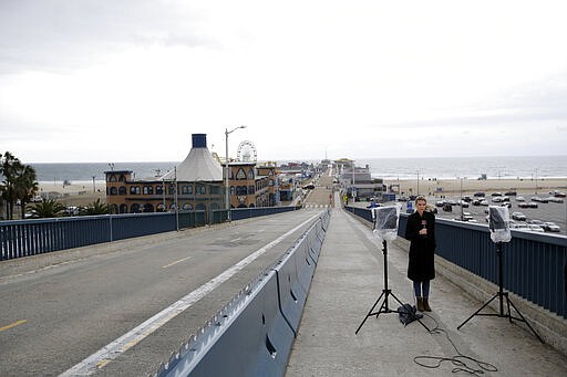 A reporter gets ready to broadcast at a near-empty Santa Monica Pier after a temporary closure as part of measures to combat the spread of the coronavirus Monday, March 16, 2020, in Los Angeles. (AP Photo/Marcio Jose Sanchez)