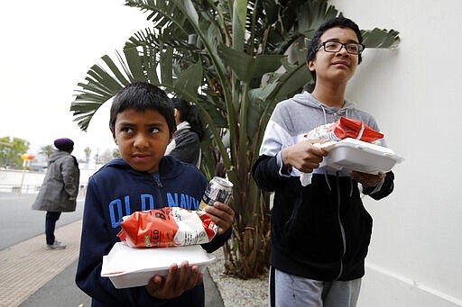 Abraham Polanco, left, and his brother Matthew Polanco receive lunches at a food distribution center set up by the Dream Center for those in need due to the coronavirus outbreak, Monday, March 16, 2020, in Los Angeles. (AP Photo/Marcio Jose Sanchez)