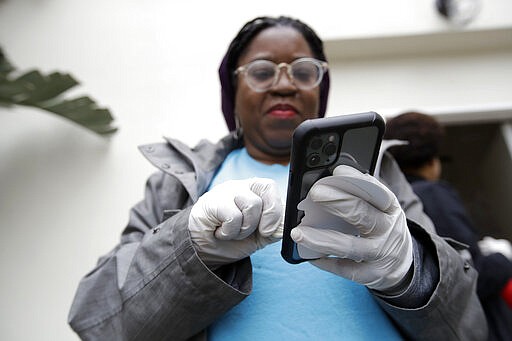 Millie Phaeton wears gloves as she checks her cell phone while volunteering at a food distribution center set up by the Dream Center Monday, March 16, 2020, in Los Angeles. (AP Photo/Marcio Jose Sanchez)