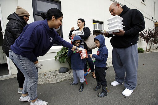 Volunteer, Pahola Campos, second from left, hands out lunches to the Garcia family, mom Marie, top center, dad Sergio, at right, David, bottom center in glasses, and Daniel at a food distribution center set up by the Dream Center for those in need due to the coronavirus outbreak, Monday, March 16, 2020, in Los Angeles. (AP Photo/Marcio Jose Sanchez)