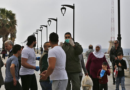 A municipal policeman, center, orders people to leave the waterfront promenade, along the Mediterranean Sea, as the country's top security council and the government were meeting over the spread of the new coronavirus, in Beirut, Lebanon, in Beirut, Lebanon, Sunday, March 15, 2020. For most people, the new coronavirus causes only mild or moderate symptoms. For some it can cause more severe illness. (AP Photo/Hussein Malla)