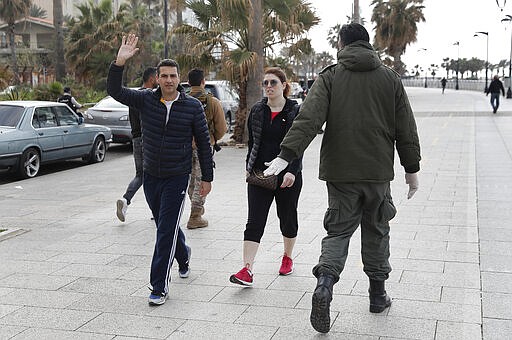 A municipal policeman, right, orders people to leave the waterfront promenade, along the Mediterranean Sea, as the country's top security council and the government were meeting over the spread of the new coronavirus, in Beirut, Lebanon, in Beirut, Lebanon, Sunday, March 15, 2020. For most people, the new coronavirus causes only mild or moderate symptoms. For some it can cause more severe illness. (AP Photo/Hussein Malla)