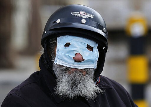 A man with a motorcycle helmet covers his face with a mask, as he watches municipal policemen order people to leave the corniche, or waterfront promenade, along the Mediterranean Sea, as the country's top security council and the government were meeting over the spread of coronavirus, in Beirut, Lebanon, in Beirut, Lebanon, Sunday, March 15, 2020.  (AP Photo/Hussein Malla)