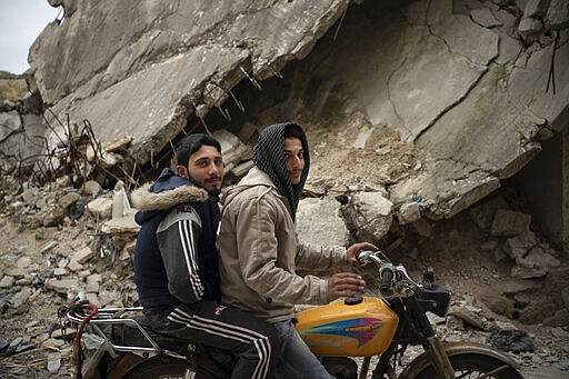 In this Thursday, March 12, 2020 photo, two Syrians pose for a photo as they ride a motorcycle in a neighborhood heavily damaged by airstrikes, in Idlib, Syria. Idlib city is the last urban area still under opposition control in Syria, located in a shrinking rebel enclave in the northwestern province of the same name. Syria&#146;s civil war, which entered its 10th year Monday, March 15, 2020, has shrunk in geographical scope -- focusing on this corner of the country -- but the misery wreaked by the conflict has not diminished. (AP Photo/Felipe Dana)